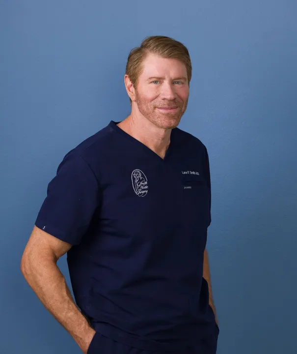 An individual in navy blue scrubs stands against a plain blue background, smiling with hands in pockets. No claims intended. Nevada Stem Cell